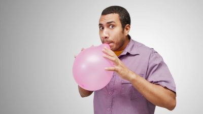A man looks nervous as he inflates a balloon, scared it might pop.