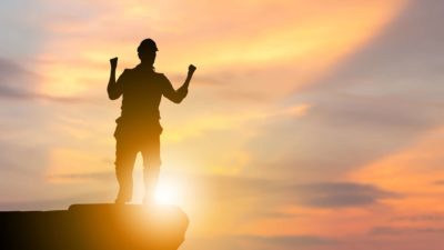 A mining worker clenches his fists celebrating success at sunset in the mine.