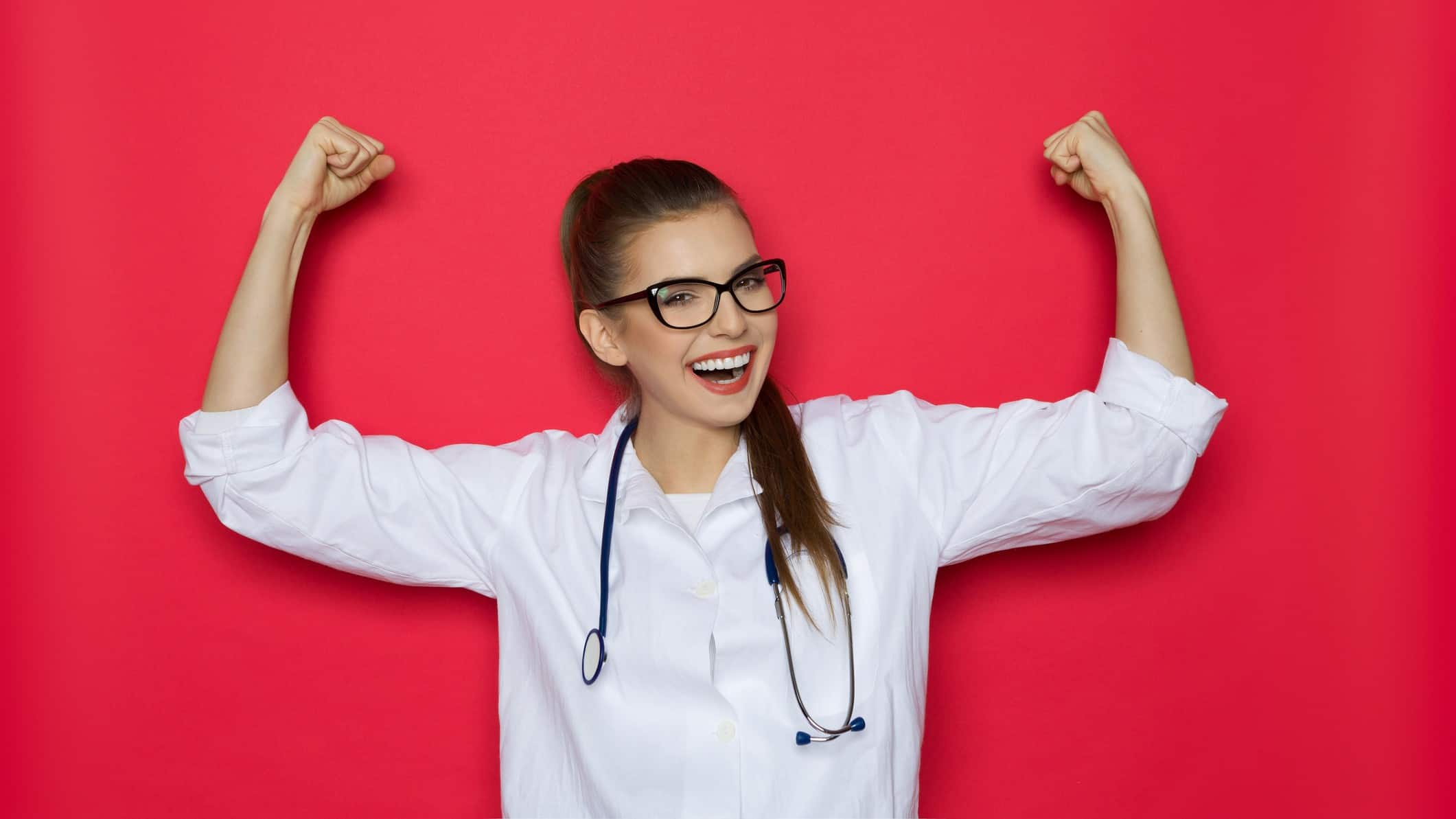 A scientist in a white coat and glasses puts her arms in the air in a sign of strength and success.