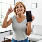 A woman shows her phone screen and points up.
