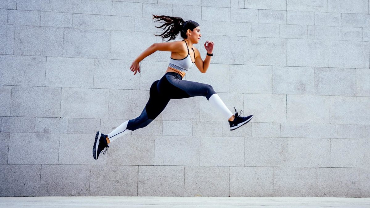 A strong female athlete powers up as she runs and leaps into the air.