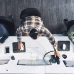Looking down on a workstation with three people working on their tech devices.