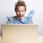 A man sitting at a computer is blown away by what he's seeing on the screen, hair and tie whooshing back as he screams argh in panic.