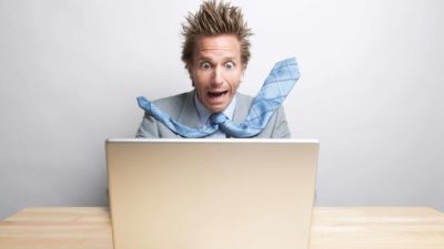 A man sitting at a computer is blown away by what he's seeing on the screen, hair and tie whooshing back as he screams argh in panic.