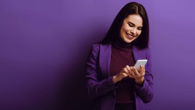 Happy woman in purple clothes looking at asx share price on mobile phone