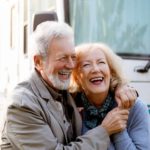 An older couple hug and smile in front of a motorhome.