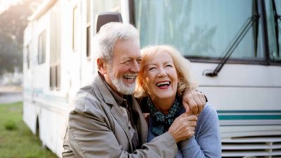 An older couple hug and smile in front of a motorhome.