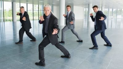 Four businessmen pull martial arts stances as they get into a defensive position.