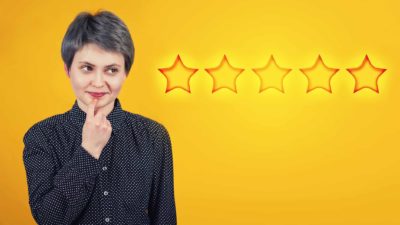 A woman has a quizzical look on her face as though she is deciding something in the foreground of a backdrop featuring five stars, like the Australian five star energy rating system.