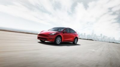 A Tesla car on a road with a wide background.