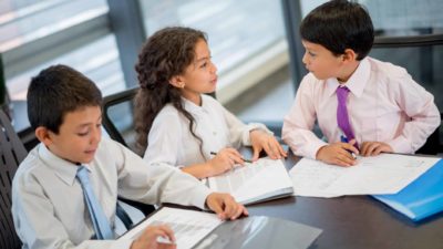 Three young people in business attire sit around a desk and discuss.