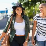 a fashionable older woman walks side by side with a stylish younger woman in a street setting as they both smile at something they are talking about.