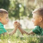 Two boys lie in the grass arm wrestling.