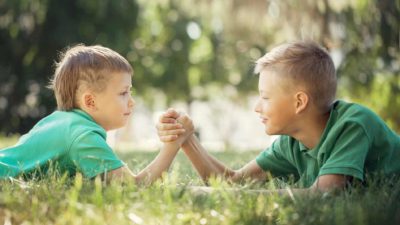 Two boys lie in the grass arm wrestling.