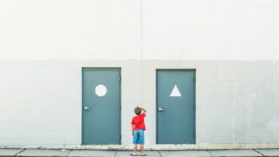 A boy stands in front of two similar but slightly different doors, scratching his head as to which one to choose.