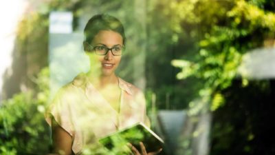 A businesswoman looks out a window at a green, environmental project.