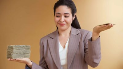 A businesswoman weighs up the stack of cash she receives, with the pile in one hand significantly more than the other hand.