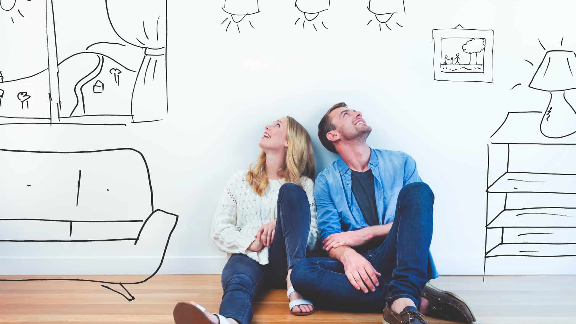 A couple sits on the floor with sketches of their dream home forming around them.