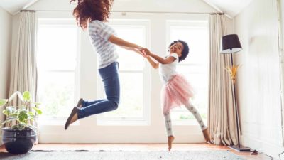 A mum and little girl leap and dance in their living room with joy.