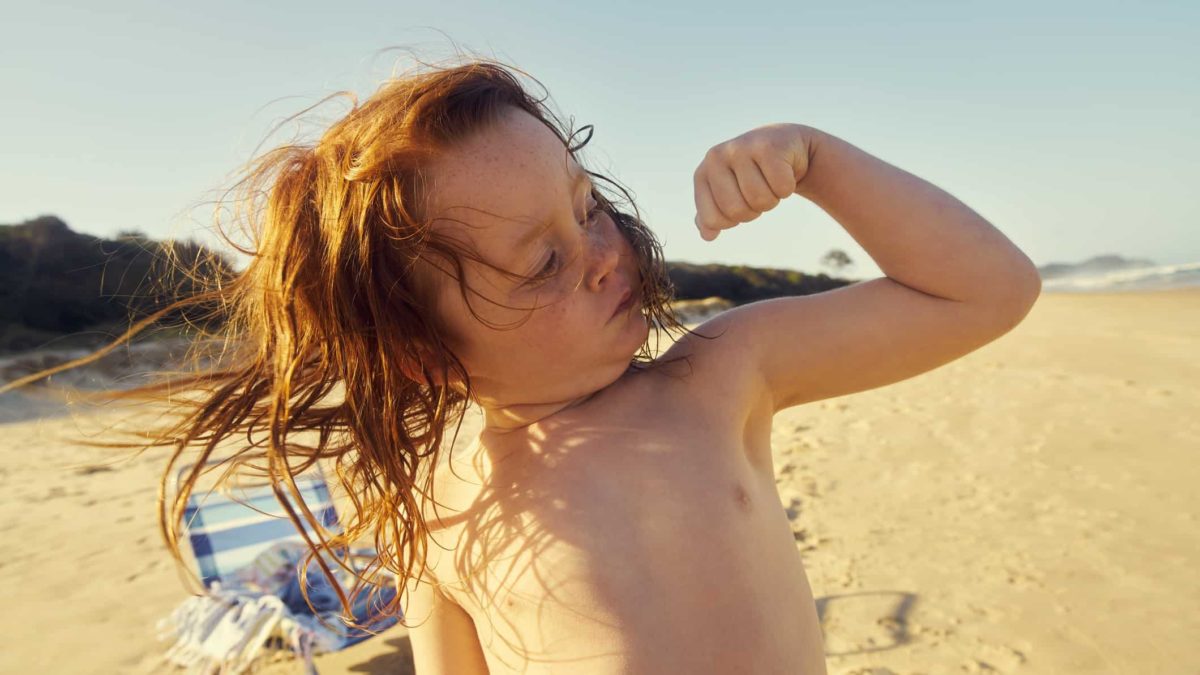 A young boy flexes his big strong muscles at the beach.