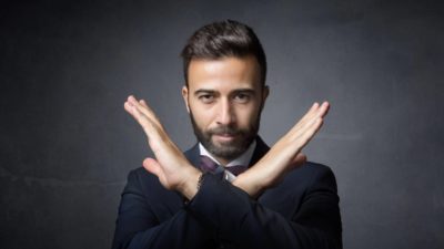 A corporate man crosses his arms to make an X, indicating no deal.