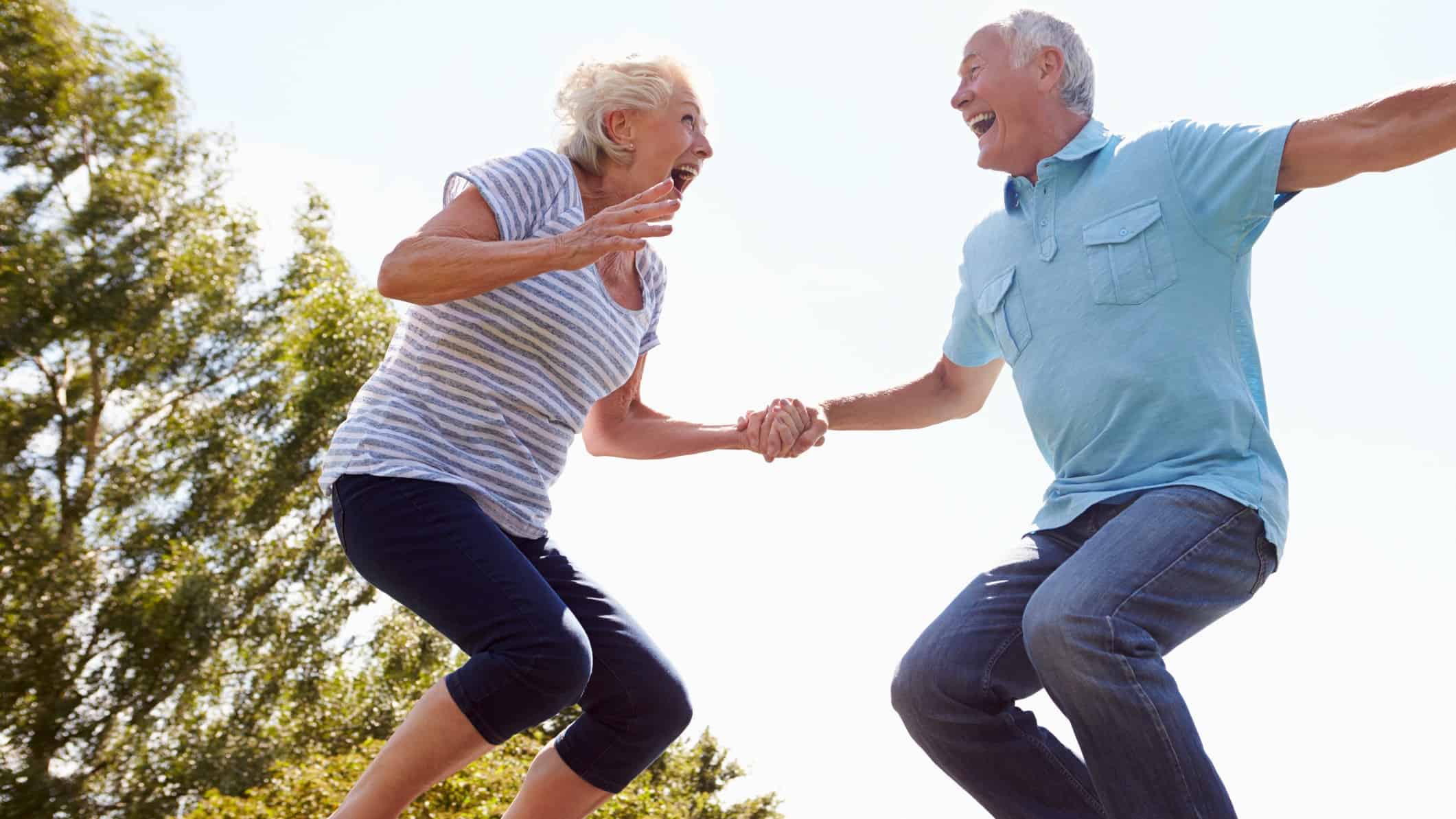 An older couple hold hands as they bounce happily high in the air.