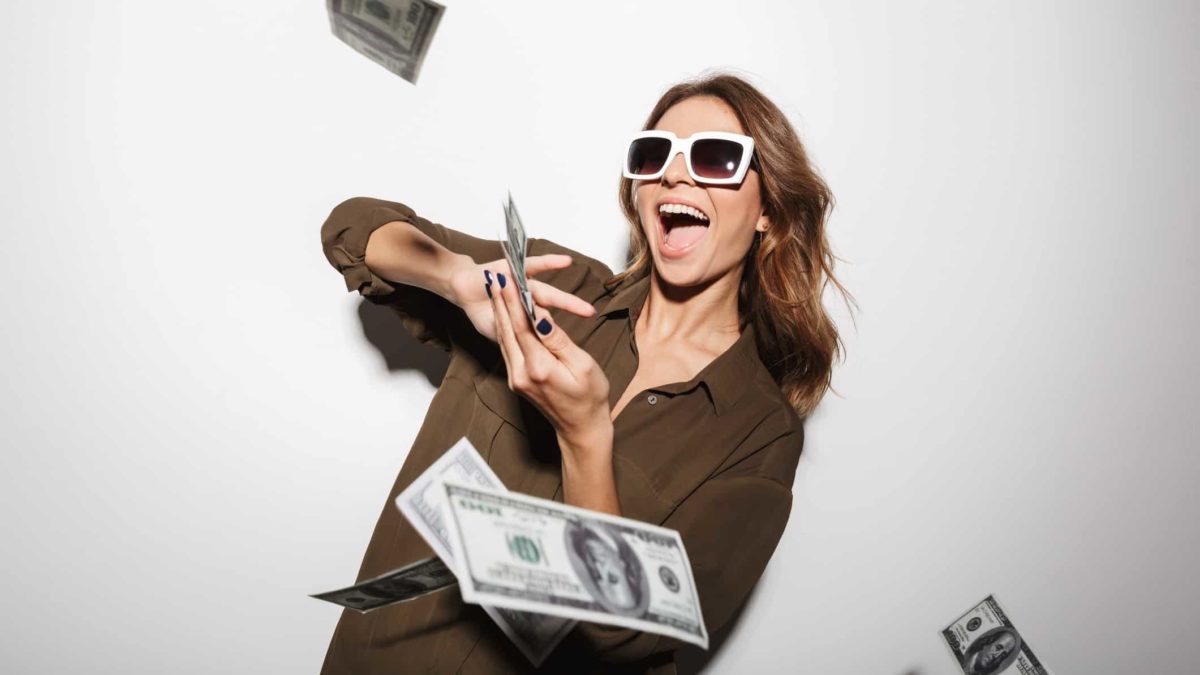 A trendy woman wearing sunglasses splashes cash notes from her hands.