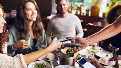 A group of friends split the bill at the restaurant after their meal, making payments on their mobile phones.