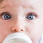 A baby's eyes open wide in surprise as it sucks on a milk bottle.