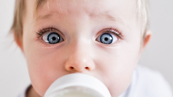 A baby's eyes open wide in surprise as it sucks on a milk bottle.