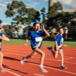 Three girls compete in a race, running fast around an athletic track.
