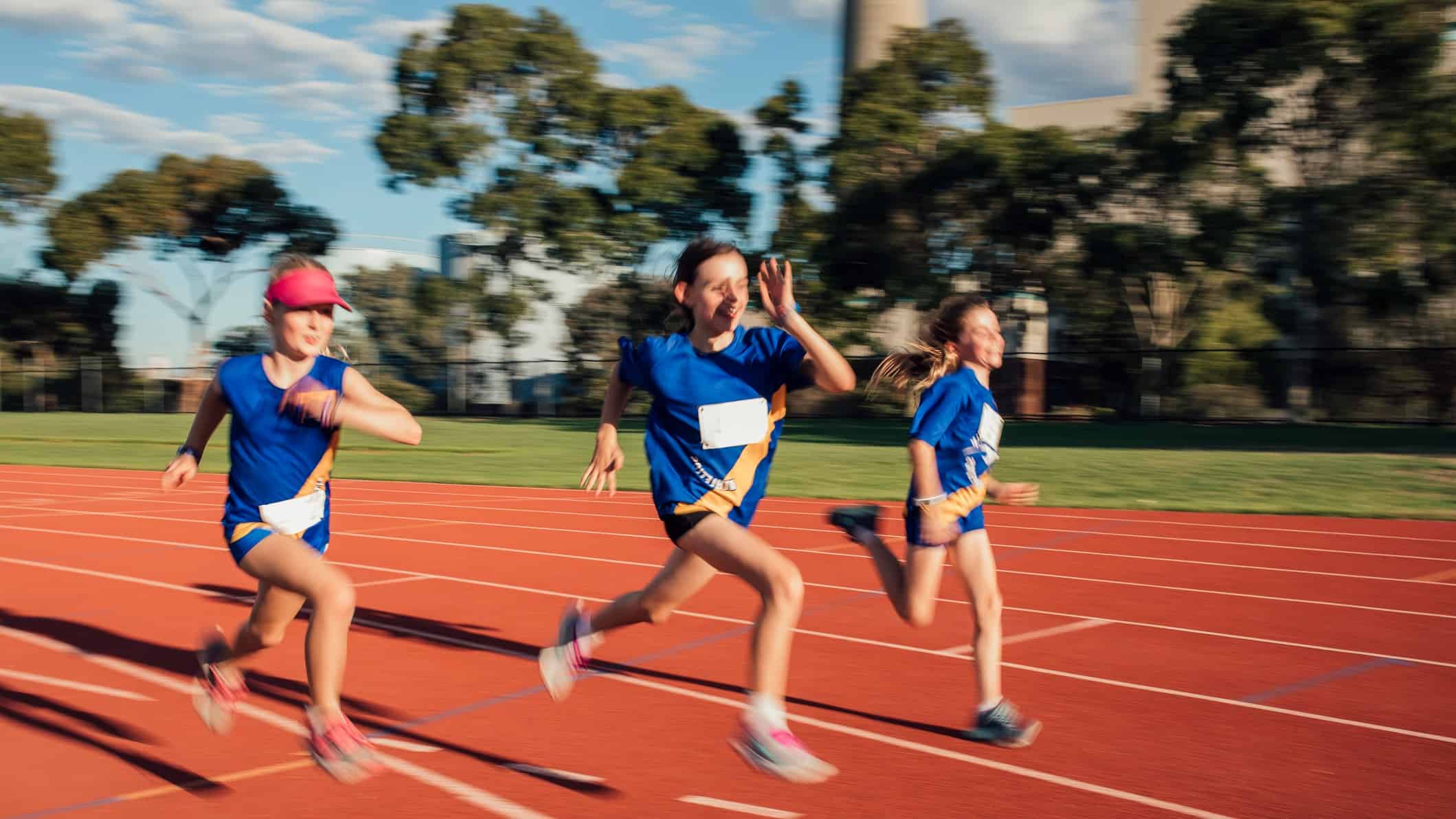 Three girls compete in a race, running fast around an athletic track.