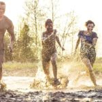 Three people run in a race through deep mud and puddles of water.