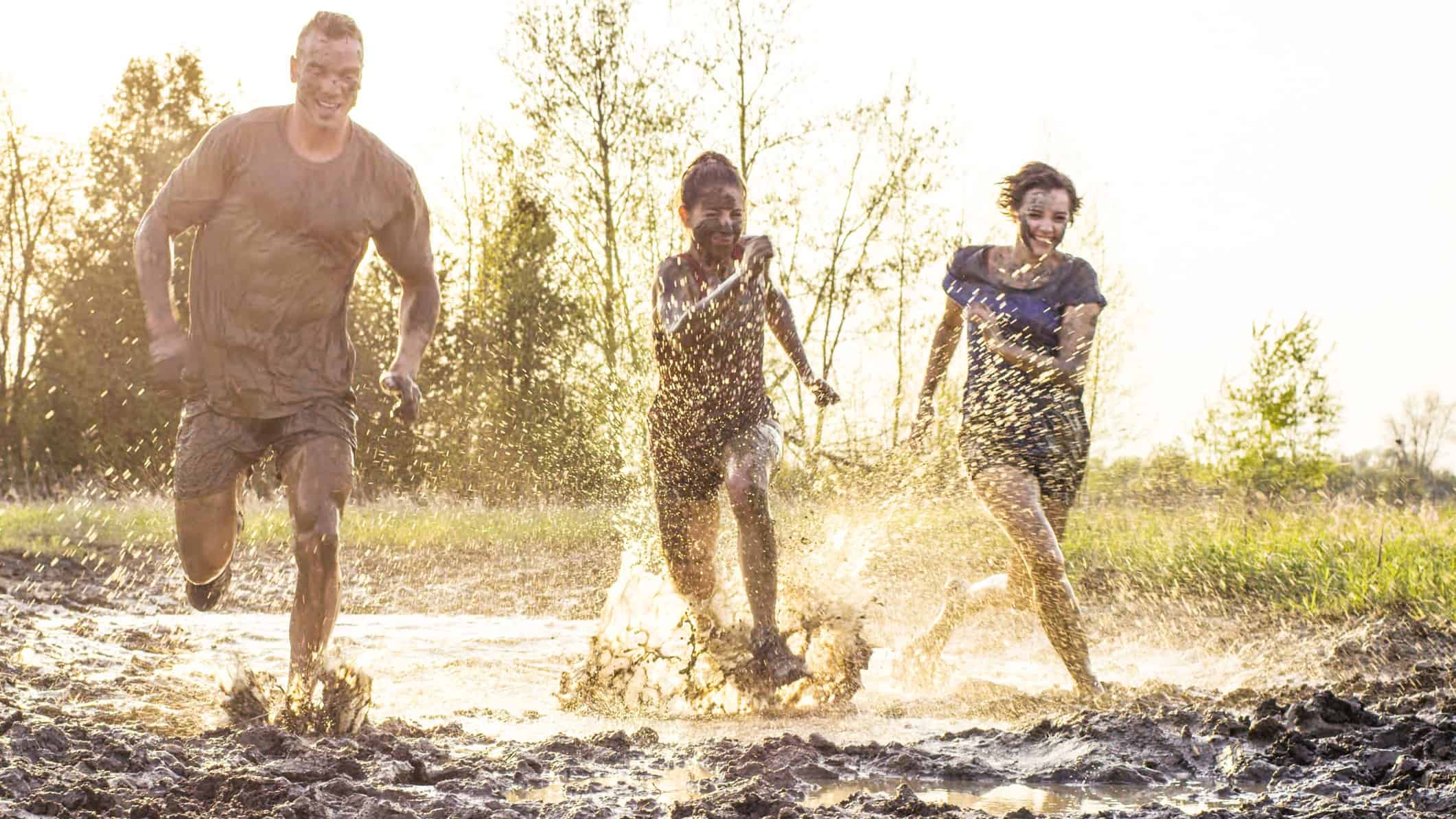 Three people run in a race through deep mud and puddles of water.