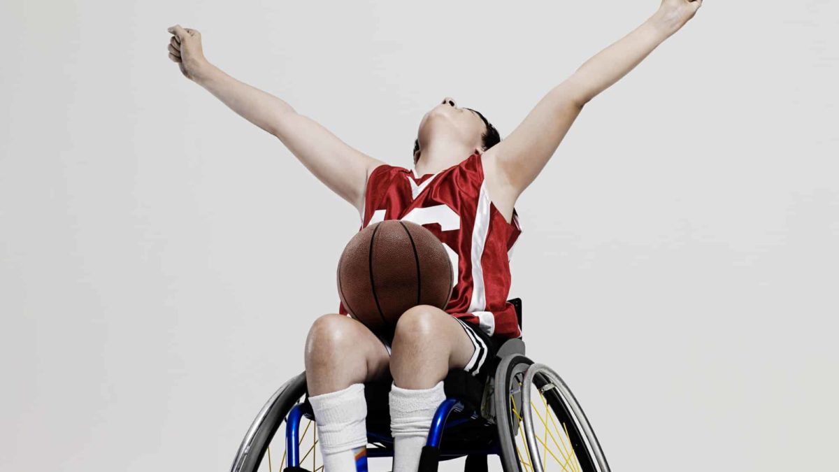A young basketballer in a wheelchair throws his arms up in triumph.