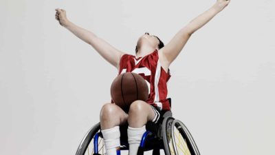A young basketballer in a wheelchair throws his arms up in triumph.