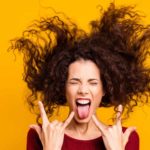 A woman pulls devil rock'n'roll hands and sticks her tongue out whilst headbanging, she's rocking it.
