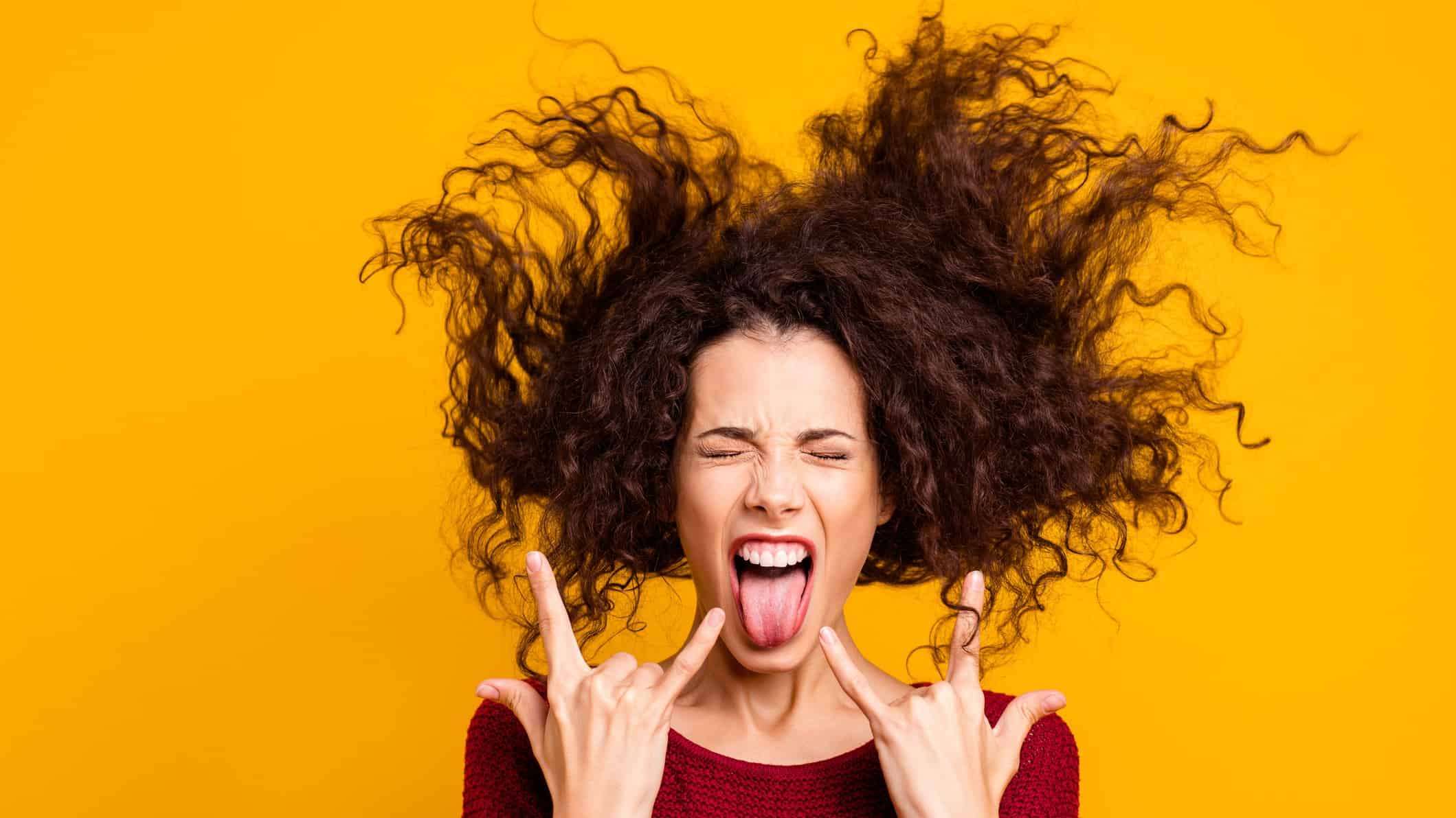 A woman pulls devil rock'n'roll hands and sticks her tongue out whilst headbanging, she's rocking it.