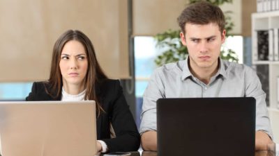 A businesswoman and businessman look sideways at each other during a dispute at their laptops.