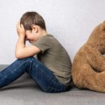 A child covering his eyes hiding from a toy bear.