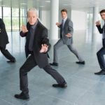 Four businessmen in suits pose together in a martial arts style pose as if ready to engage in competition or spring into a fight.