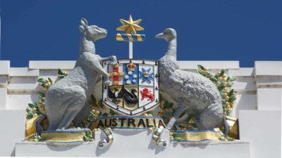 The Australian Coat of Arms flanked by a kangaroo and an emu features as a fresco on a building with the backdrop of a blue sky.