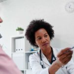 A doctor sits with a patient and uses a pen to point to certain parts of her mammogram scan