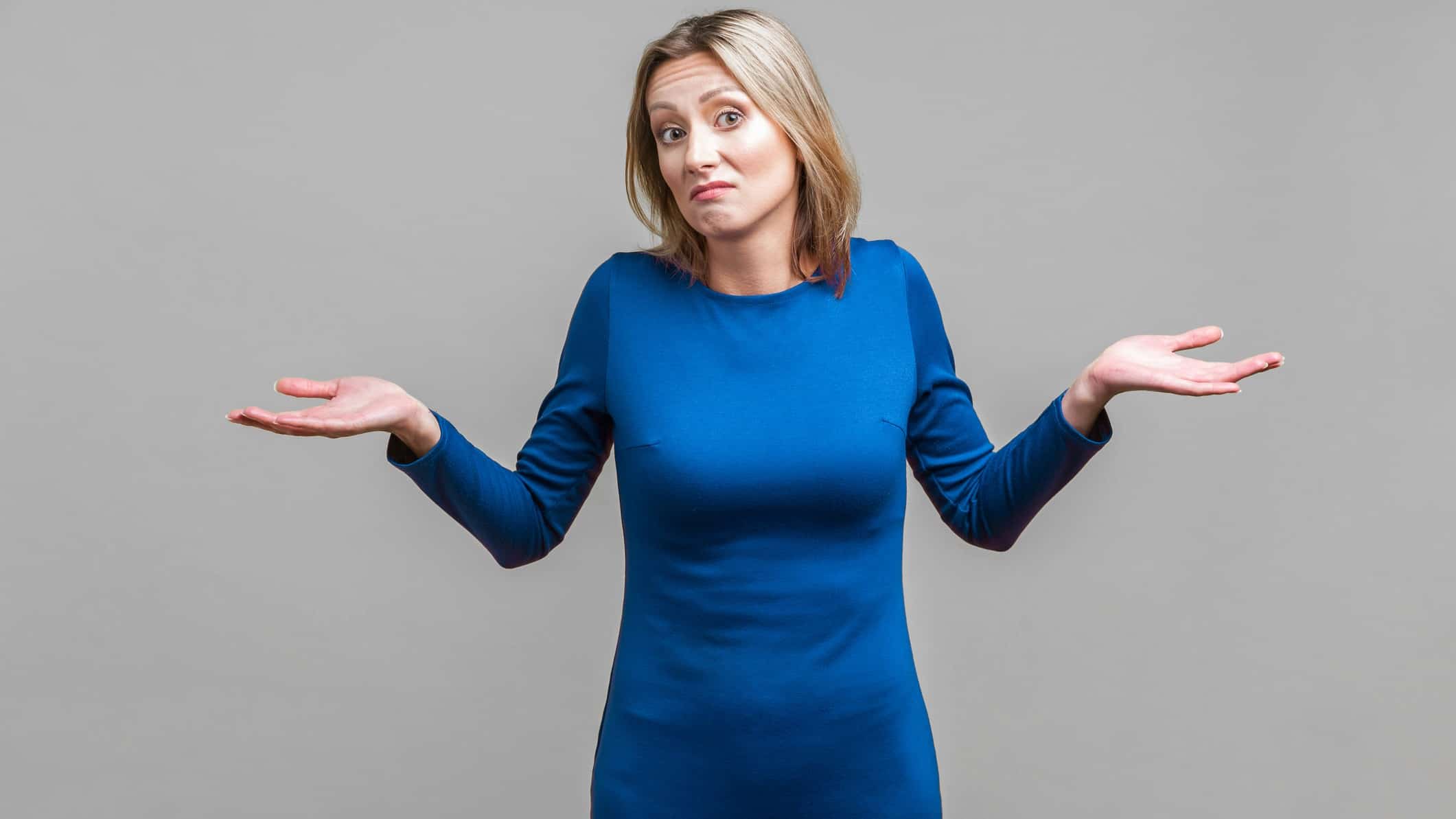 A woman in her late 30s holds her hands out either side with the palms up as if indicating she doesn't know the answer to a question. She has a quizzical look on her face.