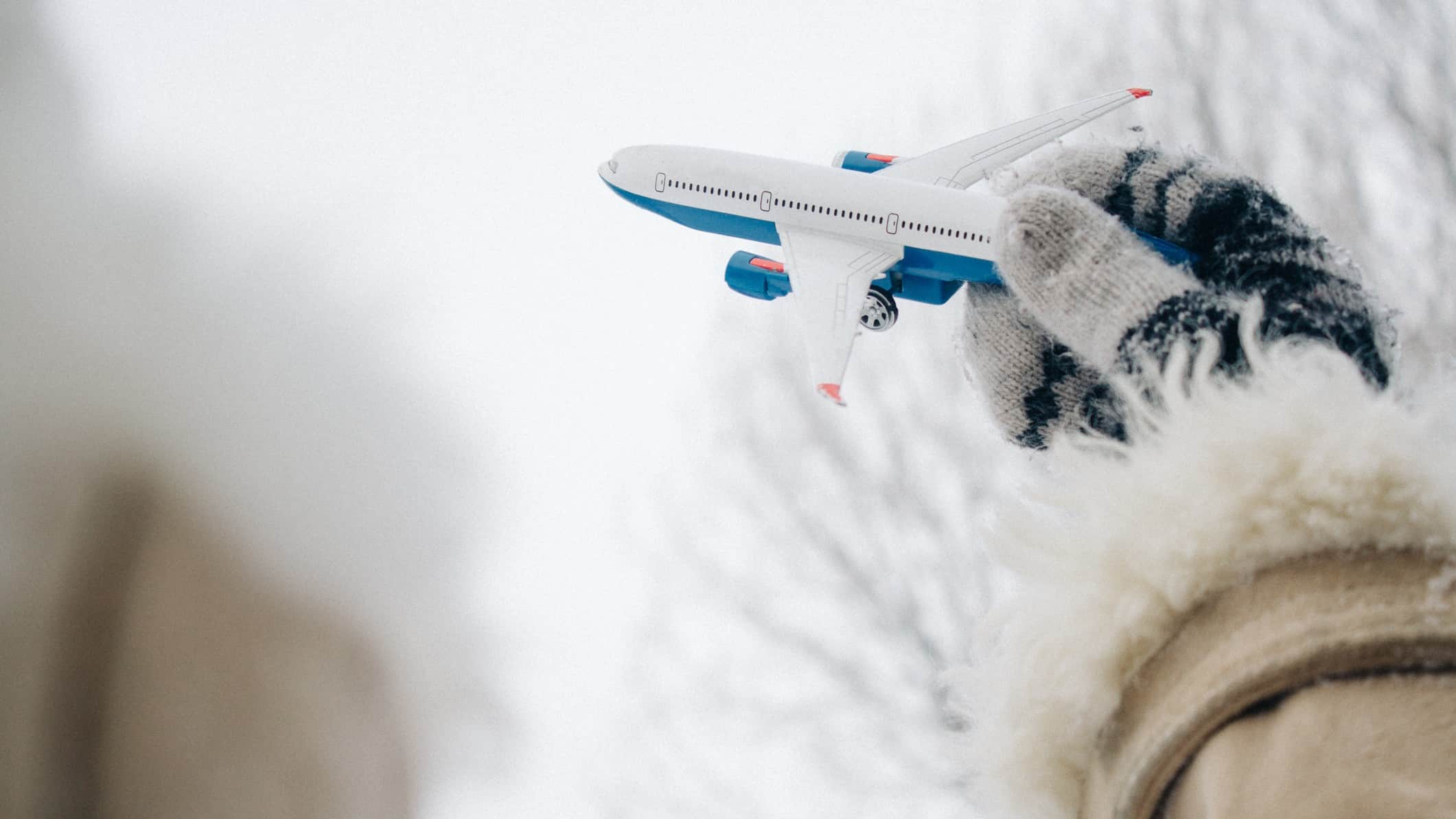 A gloved hand holds a toy metal aeroplane agains the backdrop of a snowy, icy landscape.
