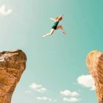 A female athlete in green spandex leaps from one cliff edge to another representing 3 ASX shares that are destined to rise and be great