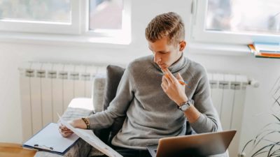 A young man sits at his desk with a laptop and documents with a gas heater visible behind him as though he is considering the information in front of him. about the BHP share price