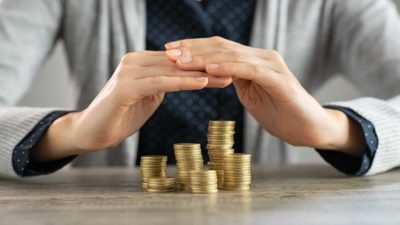 A banker uses his hands to protects a pile of coins on his desk, indicating a possible inflation hedge