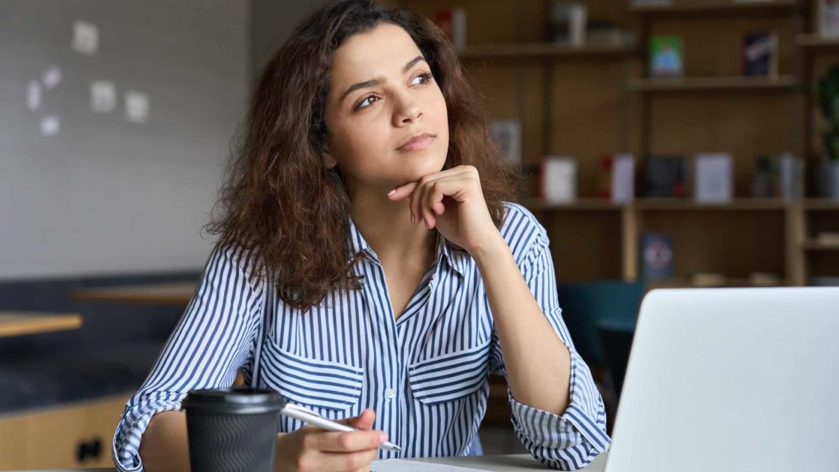 A young woman sits with her hand to her chin staring off to the side thinking about her investments.