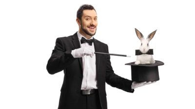 A magician wearing traditional dinner suit and white gloves holds a magic wand in one hand and a top hat in the other with a cute white bunny popping out of it, wearing a bow tie.
